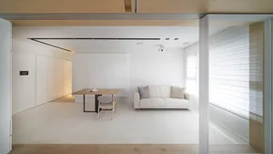 Minimalist living room with a white sofa, wooden dining table, and integrated kitchen area.