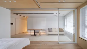 Minimalist living room with white furniture, wood floor, and large windows.