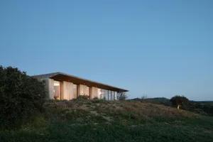 A modern house made of wood on a grassy hillside.