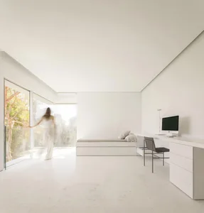 A minimalist bedroom featuring a sleek, modern bed with integrated storage, a sleek white desk, and large windows with glass 
