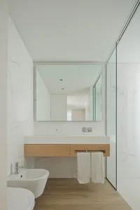 Modern bathroom featuring white marble walls, a floating wooden vanity with a white countertop, and a glass-enclosed shower a