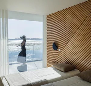 A modern bedroom featuring a bed with a wooden headboard and an ocean view.