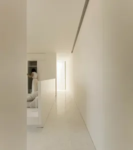 A minimalist, white-marble interior space with a hallway and bedroom.
