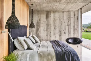 A modern bedroom with a concrete wall and a black bed frame with white bedding and pillows.