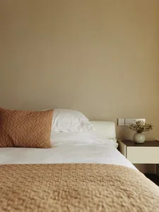 Minimalist bedroom with bed, pillows, blanket, nightstand, and vase with flowers