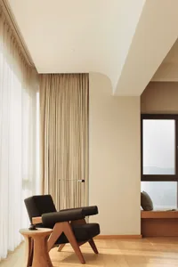A minimalist living room featuring wooden furniture and a window with curtains.