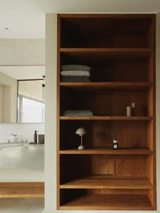 A modern bathroom with wooden shelving holding towels and decorative items.