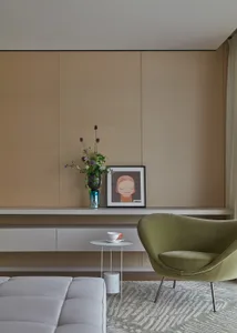 A modern living room with minimalist furniture, a green armchair, and a white sofa against a beige wall.