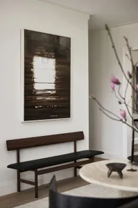 A minimalist living room features a wooden bench and a large framed artwork depicting a window reflected in water.