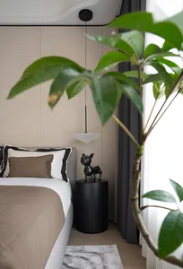 Modern bedroom featuring textured beige wall panels, dark curtains with white sheers, black bedside table, brown blanket, and