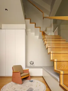 A modern living space featuring a wooden staircase with glass railings and a cushioned bench seat at the landing.