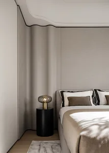 Modern minimalist bedroom featuring a bed with taupe fabric bedding and a side table with a decorative lamp.