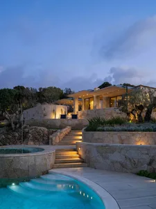 Modern minimalist house exterior with stone walls, glass windows, and wooden accents.
