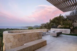 Modern residential exterior featuring a granite patio with seating and a beautiful ocean view.
