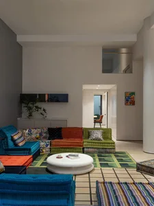 Modern living room with blue, green, and orange color scheme, featuring a round coffee table and various cushioned seating ar