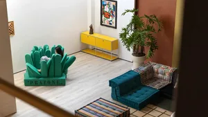 A modern living room with a large green sculptural chair and a colorful rug, featuring minimalist design elements.