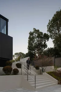 A modern staircase made of concrete with metal railings outdoors, featuring trees and bushes as a backdrop.