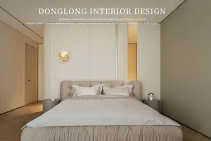 A minimalist bedroom with white walls, a beige upholstered bed, and a round gold moon art piece on the wall.
