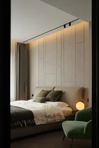 Modern bedroom featuring a fabric textured headboard, a green armchair, and ambient lighting.