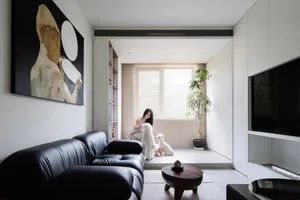 A modern minimalist living room featuring a black leather sofa, a round wooden table, and a large abstract painting on the wa
