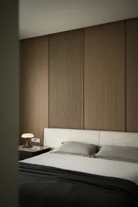 A minimalist bedroom with a white fabric headboard, textured paneling, and a wooden bedside table.