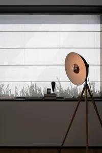 Modern minimalist interior design with white fabric blinds and wooden tripod lamp casting light through window.