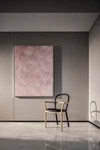 A minimalist black chair with wooden arms and a padded seat sits beside an abstract art wall in a modern interior design sett