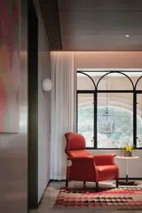 A modern lobby with a red armchair, a curtain, and a table with flowers, set against a large window.