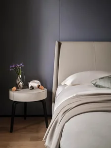A minimalist bedroom featuring a bed with a beige leather headboard and fabric bedding.
