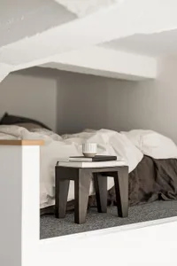 A minimalist bedroom featuring a wooden bedside table with books and a mug on top.