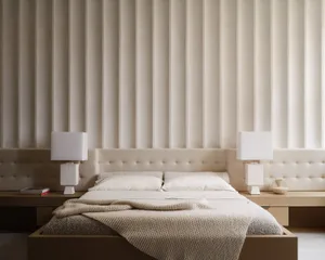 Minimalist bedroom with a white fabric bed and light-colored walls.
