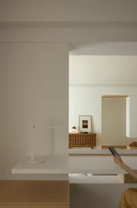 White minimalist room with a desk lamp and a person holding a smartphone.