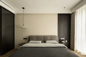 Minimalist bedroom interior featuring a bed with a upholstered headboard and grey bedding, a side table with books, and floor