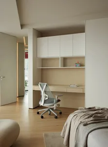 Modern minimalist master bedroom featuring a white desk with a mesh office chair, beige flooring, and light-colored wood cabi
