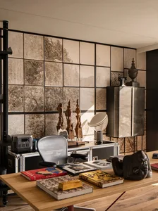 A modern, industrial-style office space featuring a wooden desk, metal shelving, and glass windows with a view of trees.