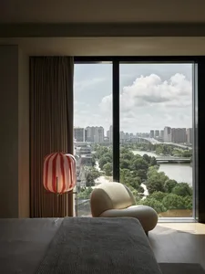 A modern view lounge with a textile chair, lamp, and window overlooking a cityscape and river.