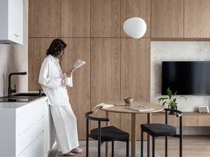 A person in minimalist-themed outfit reading a newspaper in a sleek, modern residential kitchen with wood cabinetry and black
