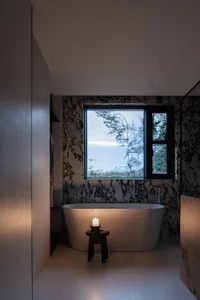 Modern minimalist bathroom featuring a freestanding tub with a candle and a view through a window with black marble wallpaper