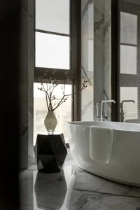 Modern bathroom with a freestanding bathtub, marble walls, and a vase with flowers on a geometric stool.