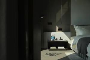 A modern, minimalist bedroom featuring a bed with a grey headboard and a wooden bedside table with books and a candle.