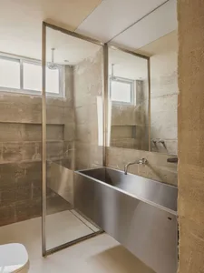A minimalist bathroom with concrete walls, a stainless steel bathtub, and a glass shower enclosure with a white floor.