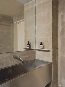 Modern, minimalist bathroom with concrete walls and a stainless steel sink.
