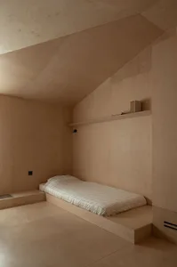 A minimalist bedroom featuring wooden walls and a low platform bed with a grid-patterned blanket.