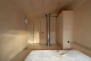A bedroom with wooden walls and a white bedspread, featuring a minimalist design.