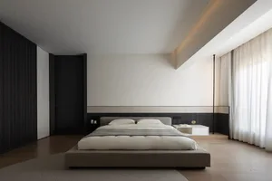 A modern minimalist bedroom with a low-profile bed, light wood flooring, and sleek white walls.