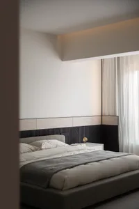 A modern minimalist bedroom with a fabric bed, white walls, and curtains.