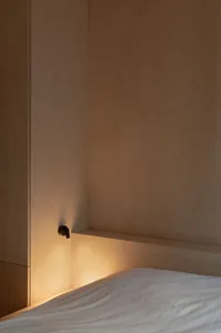 A minimalist bedroom with illuminated wood paneling and lit shelf