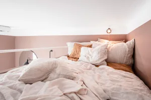A cozy bedroom featuring a bed covered in a linen-cotton blend comforter and pillows, with a warm-toned wall and ambient ligh