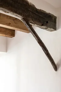 Wooden beam supporting a ceiling against a white wall, showcasing a rustic architectural design element.