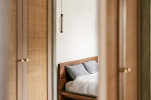 Modern minimalist bedroom featuring a wooden bed with white bedding and pillows, minimalistic design, and a hanging lamp.
